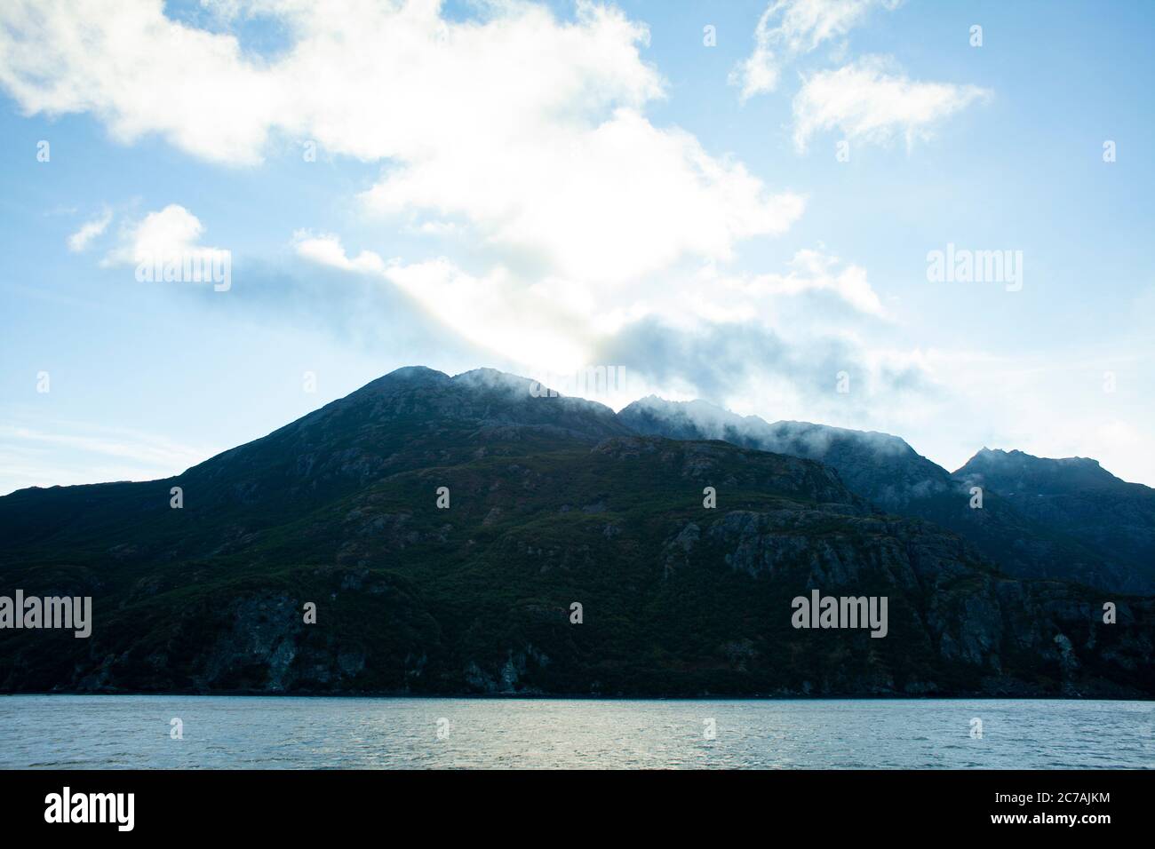 La nebbia si snoda sulle acque del lago Iliamna, Alaska, con il sole che getta luce sull'aspra silhouette di montagna e sul tranquillo paesaggio selvaggio Foto Stock