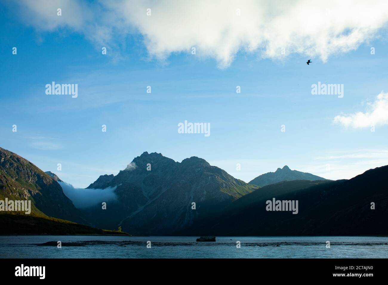 La nebbia si snoda sulle acque del lago Iliamna, Alaska, con il sole che getta luce sull'aspra silhouette di montagna e sul tranquillo paesaggio selvaggio Foto Stock