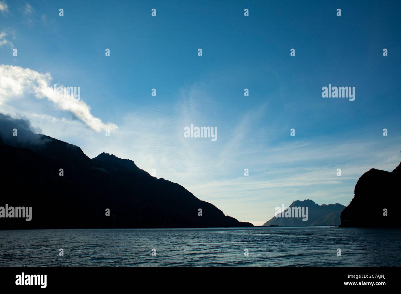 La nebbia si snoda sulle acque del lago Iliamna, Alaska, con il sole che getta luce sull'aspra silhouette di montagna e sul tranquillo paesaggio selvaggio Foto Stock