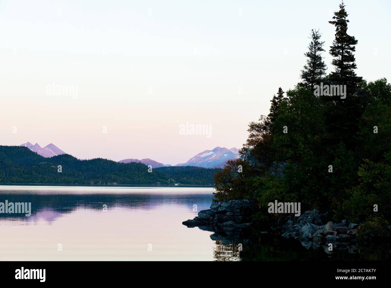 Crepuscolo sul lago Iliamna, Alaska, con acque calme che riflettono aspre coste boscose e lontane sagome di montagna nella tranquilla natura selvaggia Foto Stock