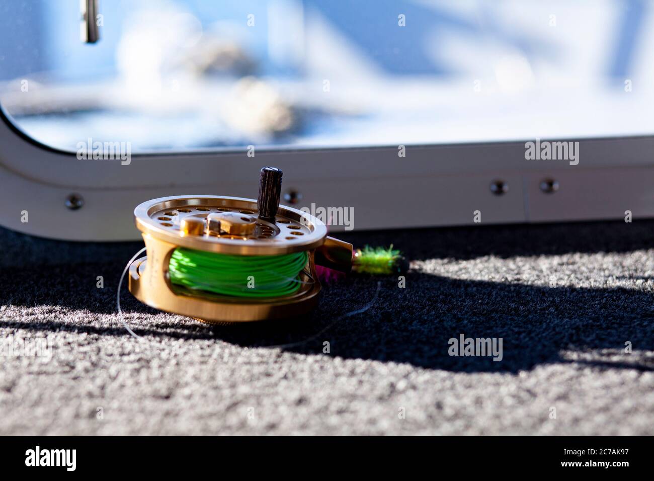 Un mulinello per la pesca con la mosca con una linea verde brillante si trova sul ponte di una barca, pronto per un'avventura di pesca in Alaska in acque incontaminate. Foto Stock