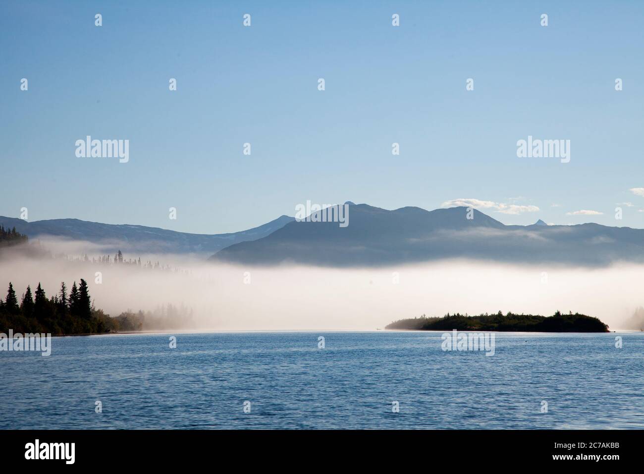 La nebbia mattutina si propaga attraverso il lago ICommanna, Alaska, con montagne sullo sfondo e luce del sole che si riflettono sulle acque tranquille e tranquille della natura selvaggia Foto Stock