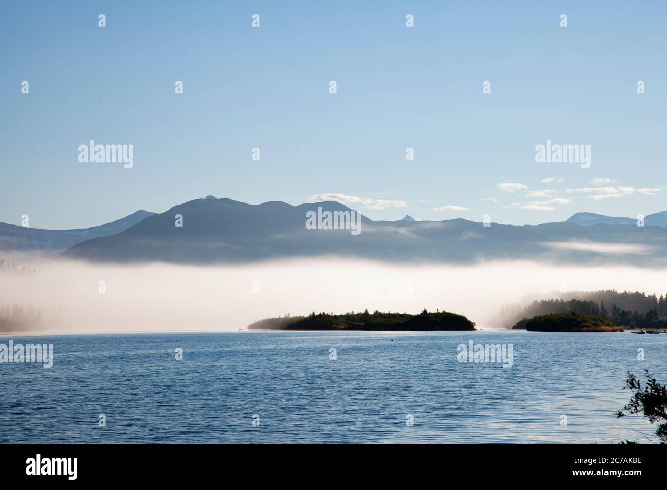 La nebbia mattutina si propaga attraverso il lago ICommanna, Alaska, con montagne sullo sfondo e luce del sole che si riflettono sulle acque tranquille e tranquille della natura selvaggia Foto Stock