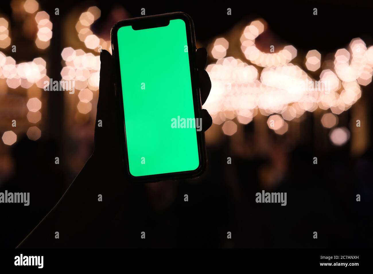 primo piano tenendo una mano con lo smartphone con schermo verde di notte. Splendido sfondo dorato bokeh Foto Stock