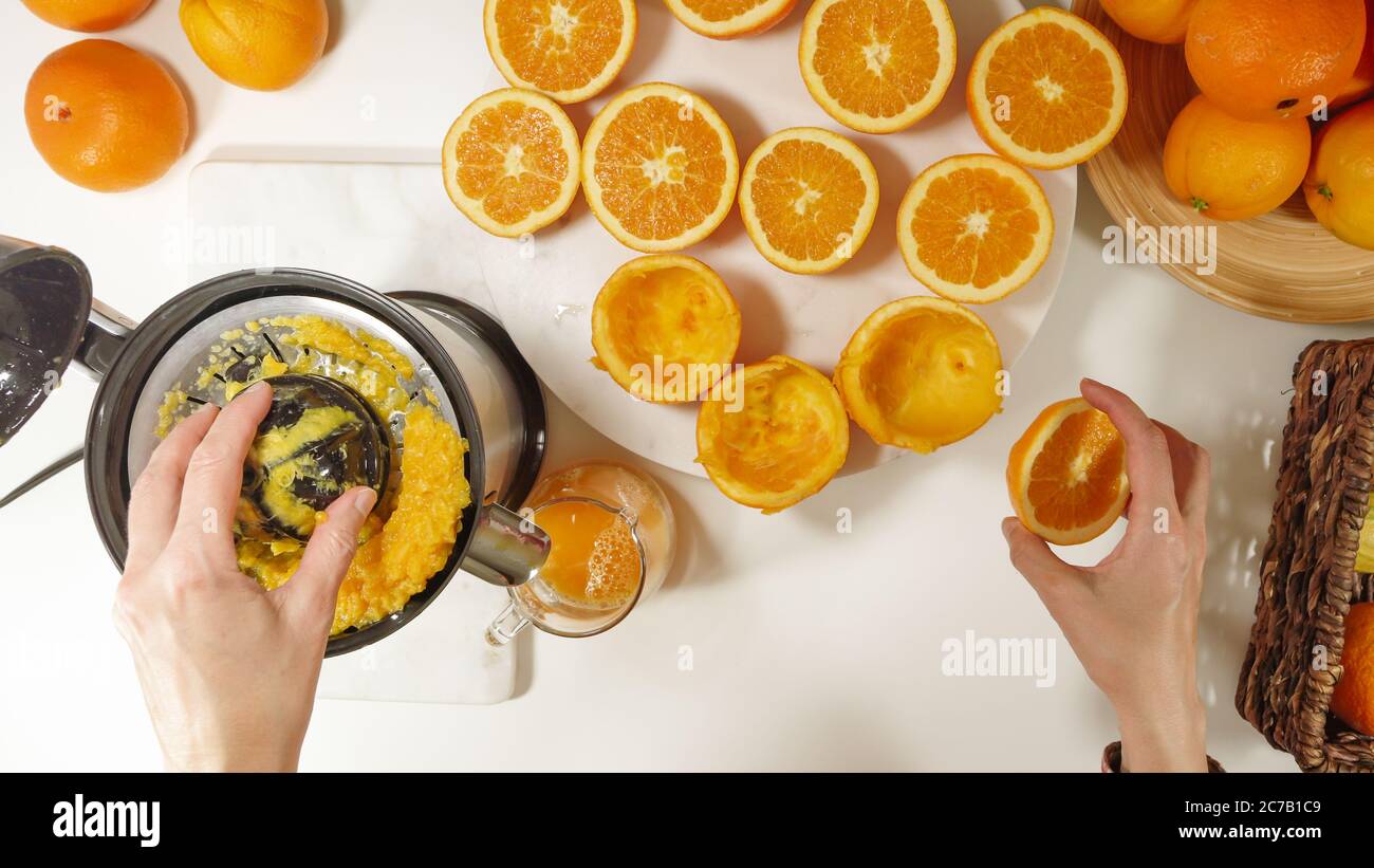Succo d'arancia appena spremuto. Donna caucasica che spremono le arance utilizzando la centrifuga elettrica. Primo piano su sfondo bianco, vista dall'alto Foto Stock