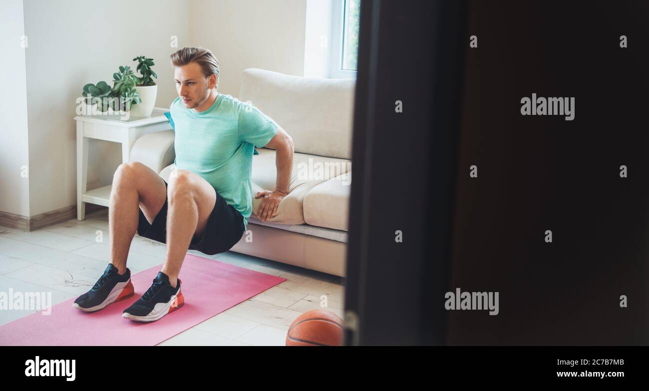 L'uomo caucasico biondo che indossa gli sportswear sta facendo il fitness a casa Foto Stock