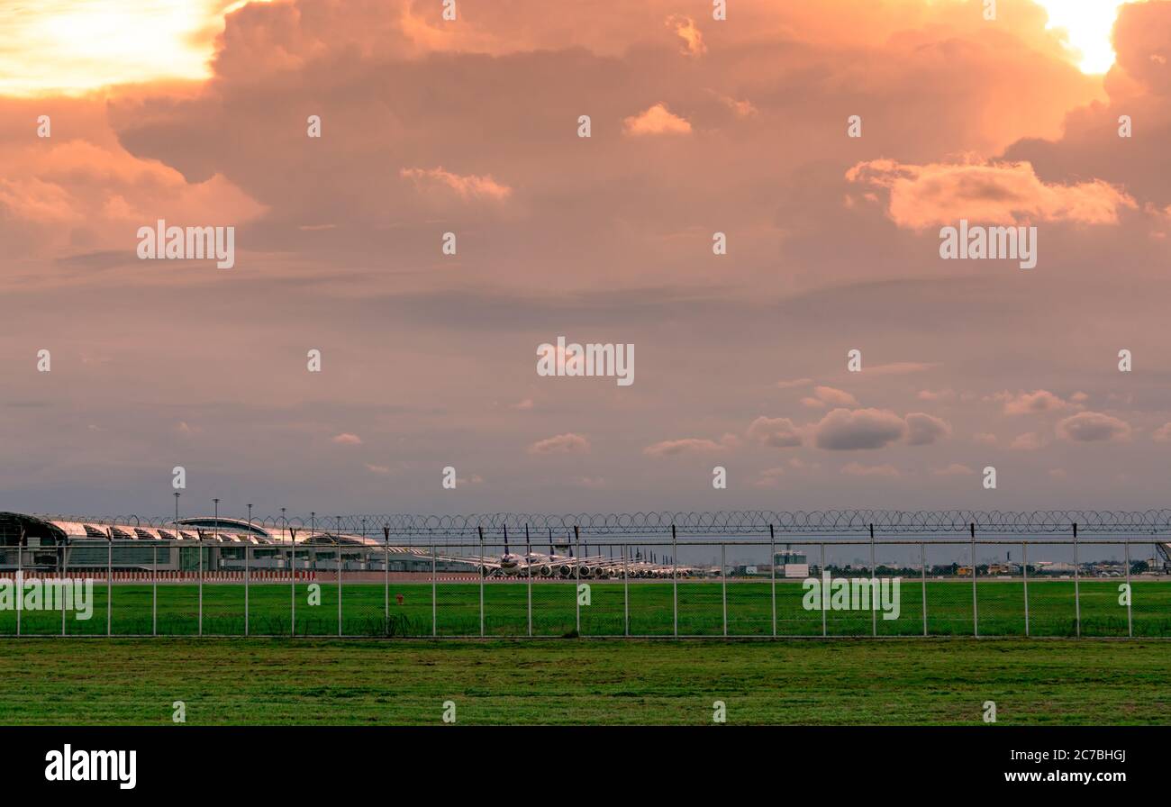 Paesaggio di verde erba campo e recinto dell'aeroporto e bellissimo cielo tramonto. Aereo commerciale parcheggiato al grembiule dell'aeroporto. Impatto del coronavirus Foto Stock