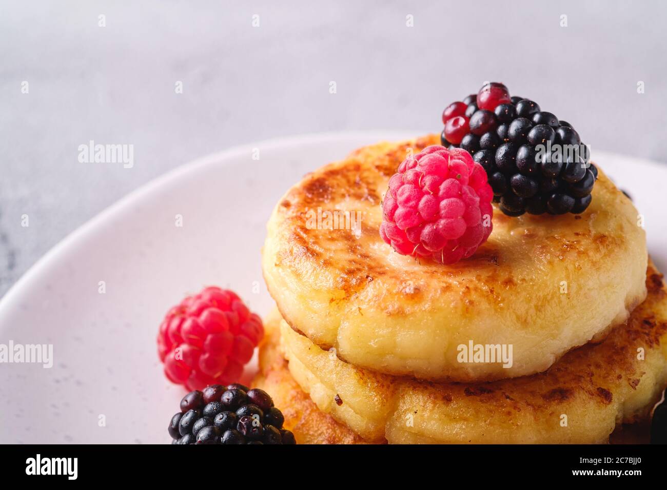 Frittelle al formaggio di cottage, frittelle di cagliata dessert con lampone e frutti di mora in piastra su fondo di pietra in cemento, macro angolo vista Foto Stock