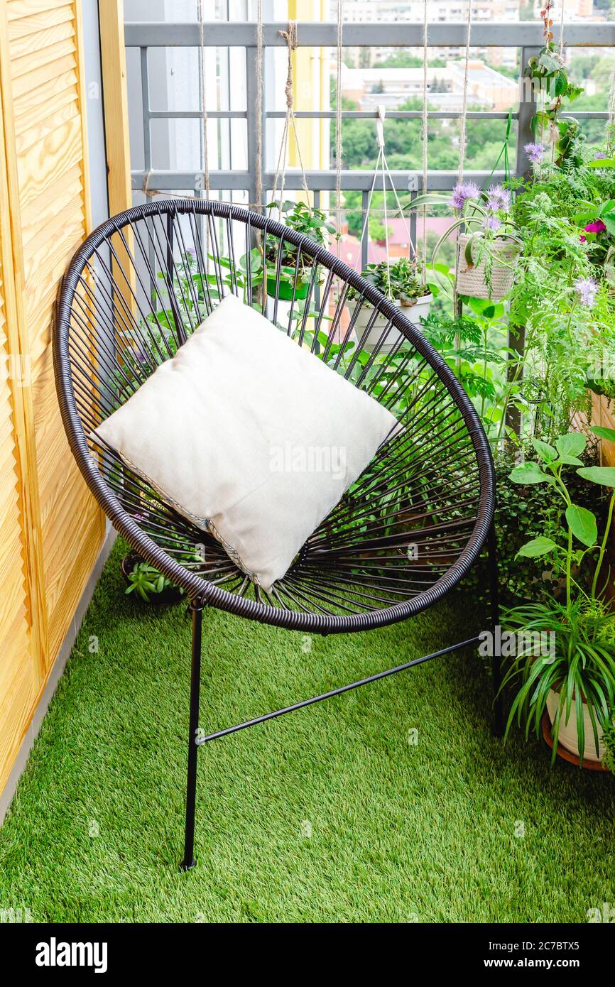 Sedia da giardino con cuscino sul balcone a casa in appartamento su prato prato con fiori di piante casa. Veranda giardino con terrazza moderna. Giardinaggio domestico Foto Stock