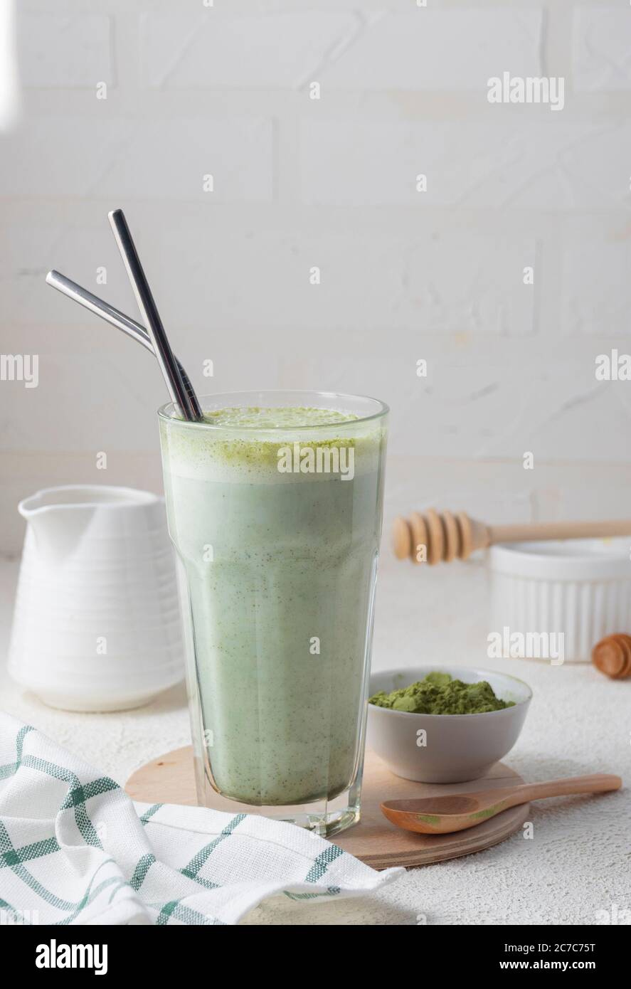 Fuoco selettivo, tè caldo matcha, latte, in vetro ad alta trasparenza e tubi metallici, con latte, in un interno domestico con piatti bianchi Foto Stock