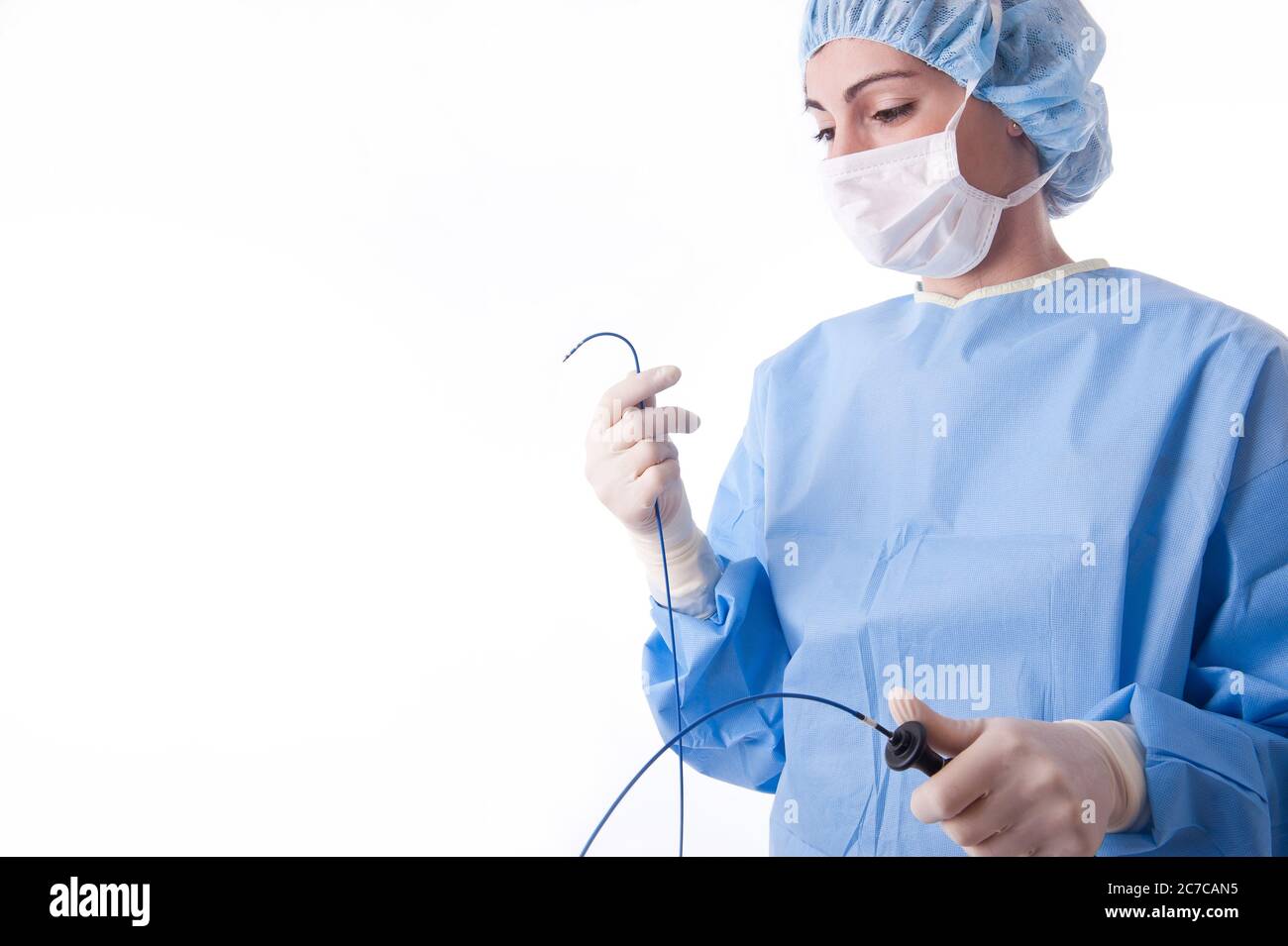 Medico o infermiere di sesso femminile che indossa una tuta o un abito sterile blu che piega un catetere per ablazione in ambiente sterile. Foto Stock