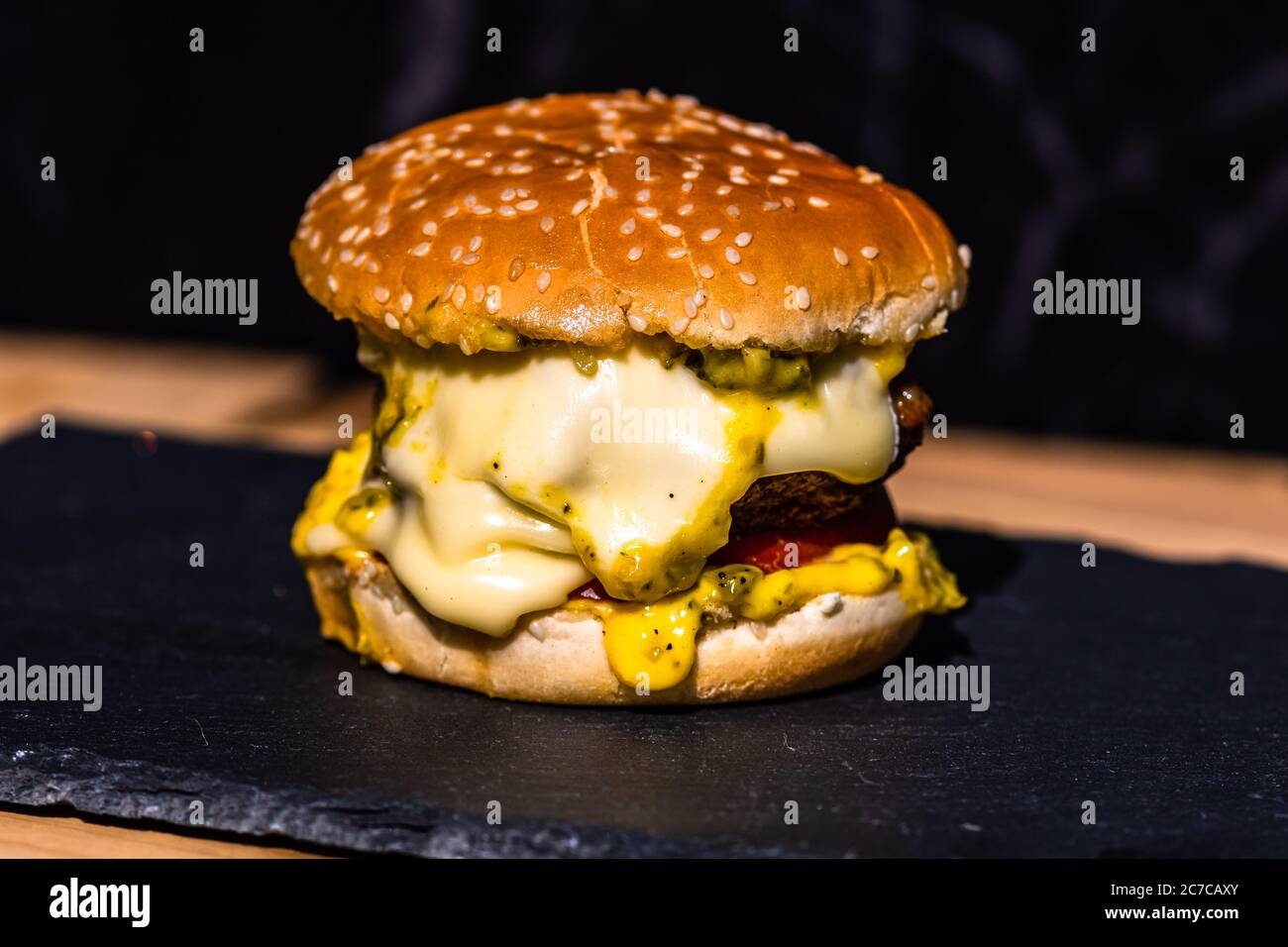 Cheeseburger di manzo fatto in casa con formaggio fuso, pomodori, cipolle, sottaceti isolati su un piatto di pietra nera. Foto Stock