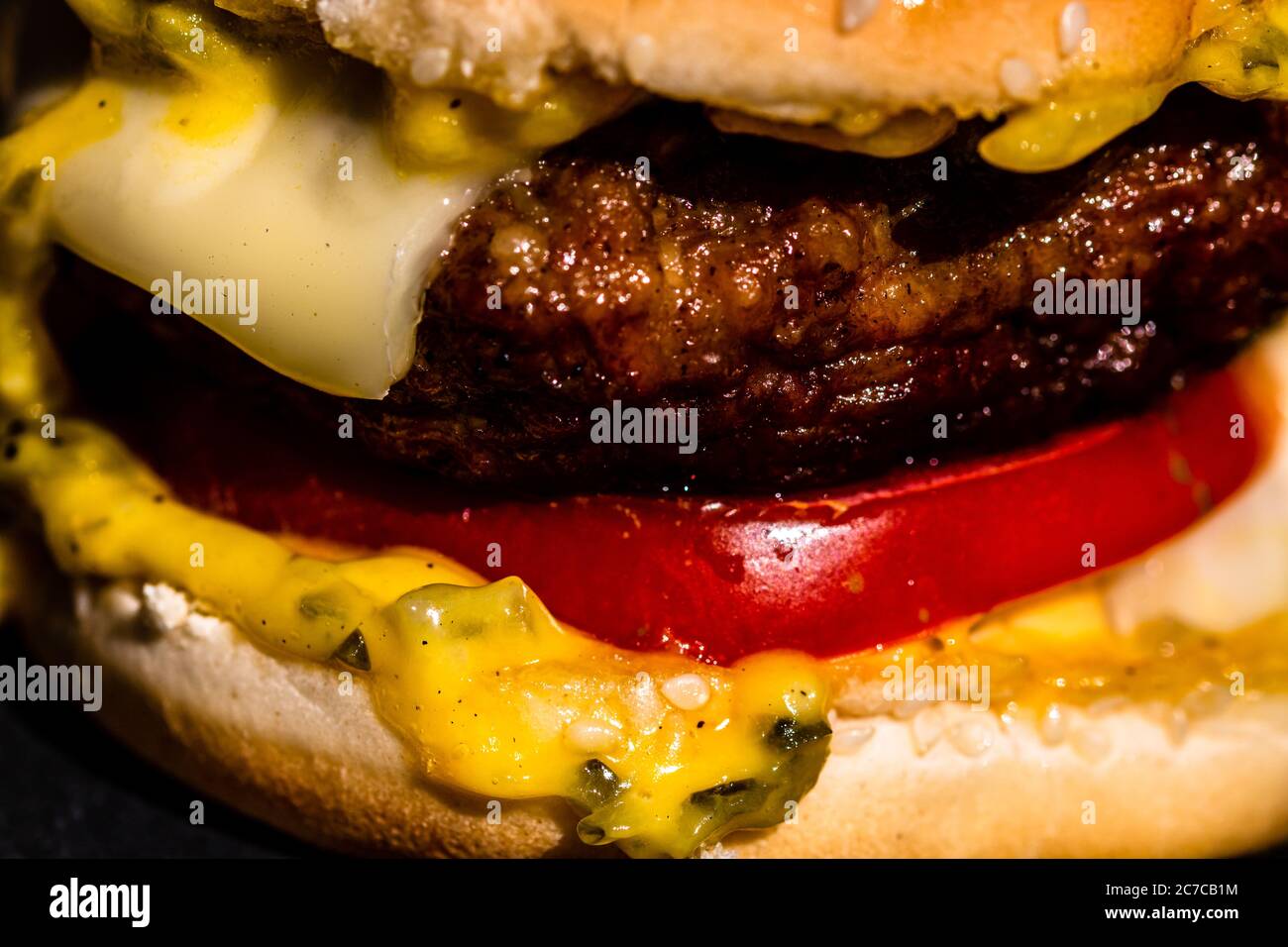 Dettaglio di cheeseburger di manzo con formaggio fuso isolato su sfondo nero. Foto Stock