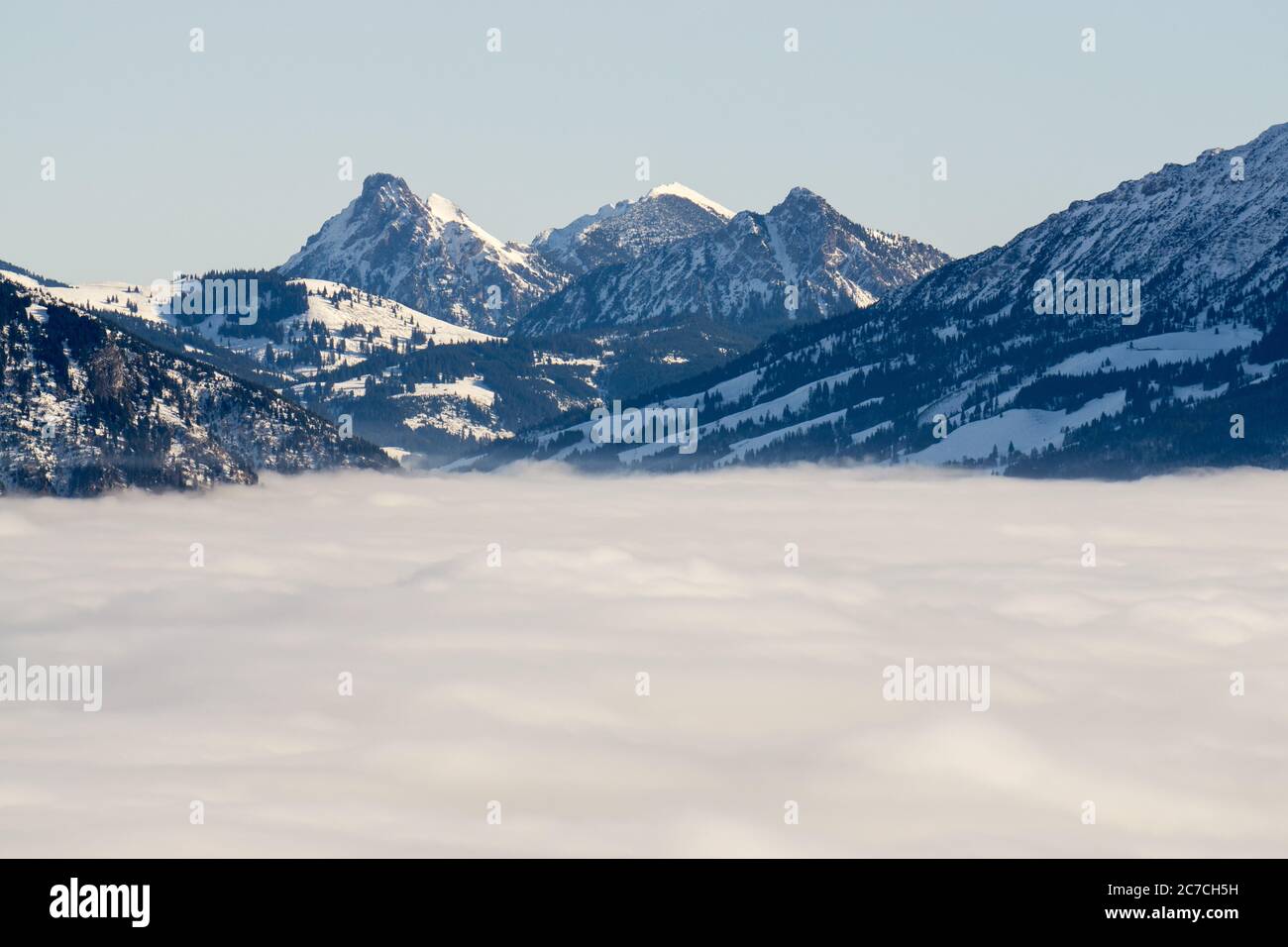Catena montuosa con neve in bassa nebbia valle con sagome. Paesaggio invernale innevato nelle Alpi, Allgau, Baviera, Germania e Tirolo, Austria. Foto Stock