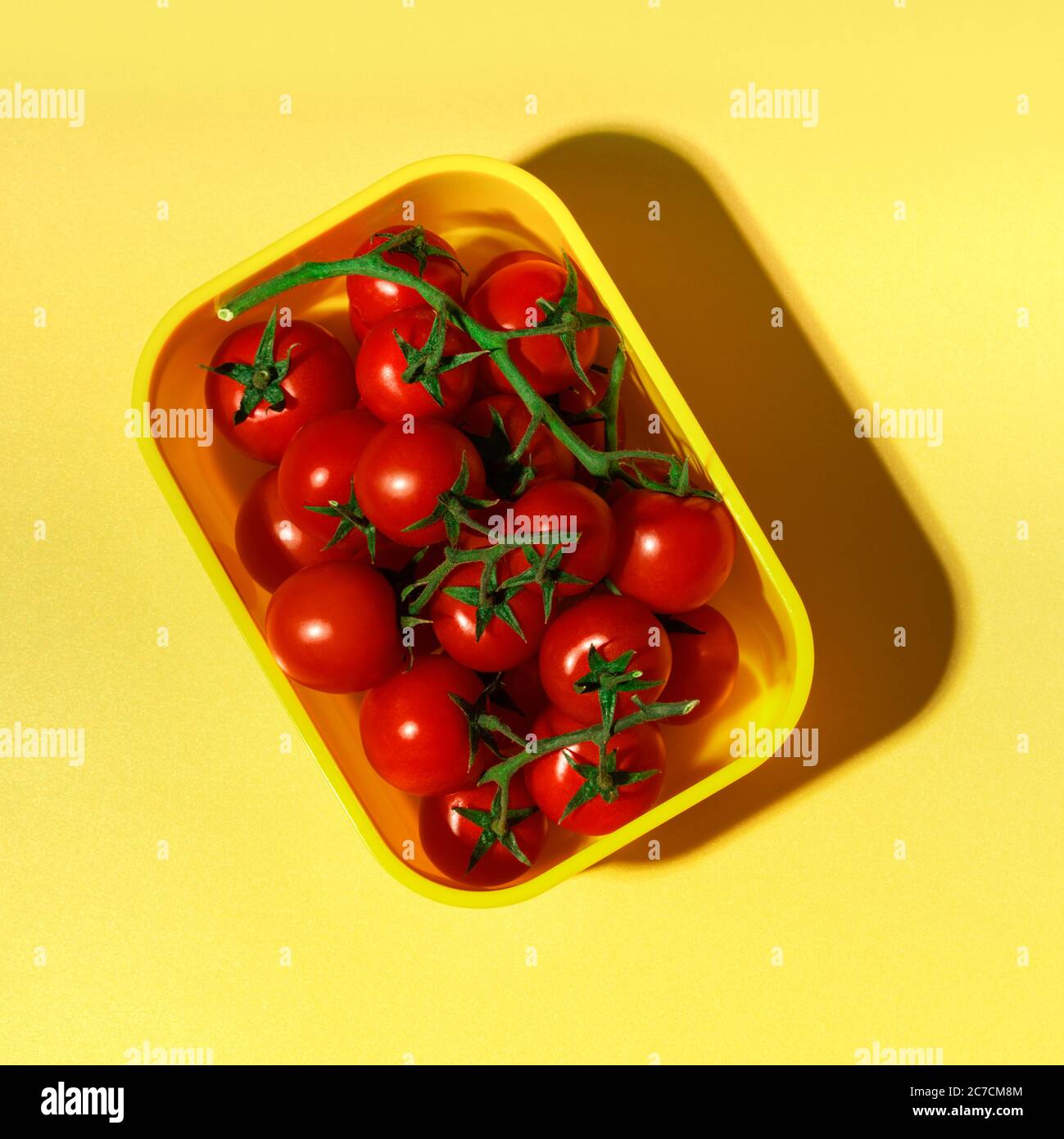 Pomodori rossi freschi in un contenitore su sfondo giallo. Fotografia quadrata, vista dall'alto. Foto Stock