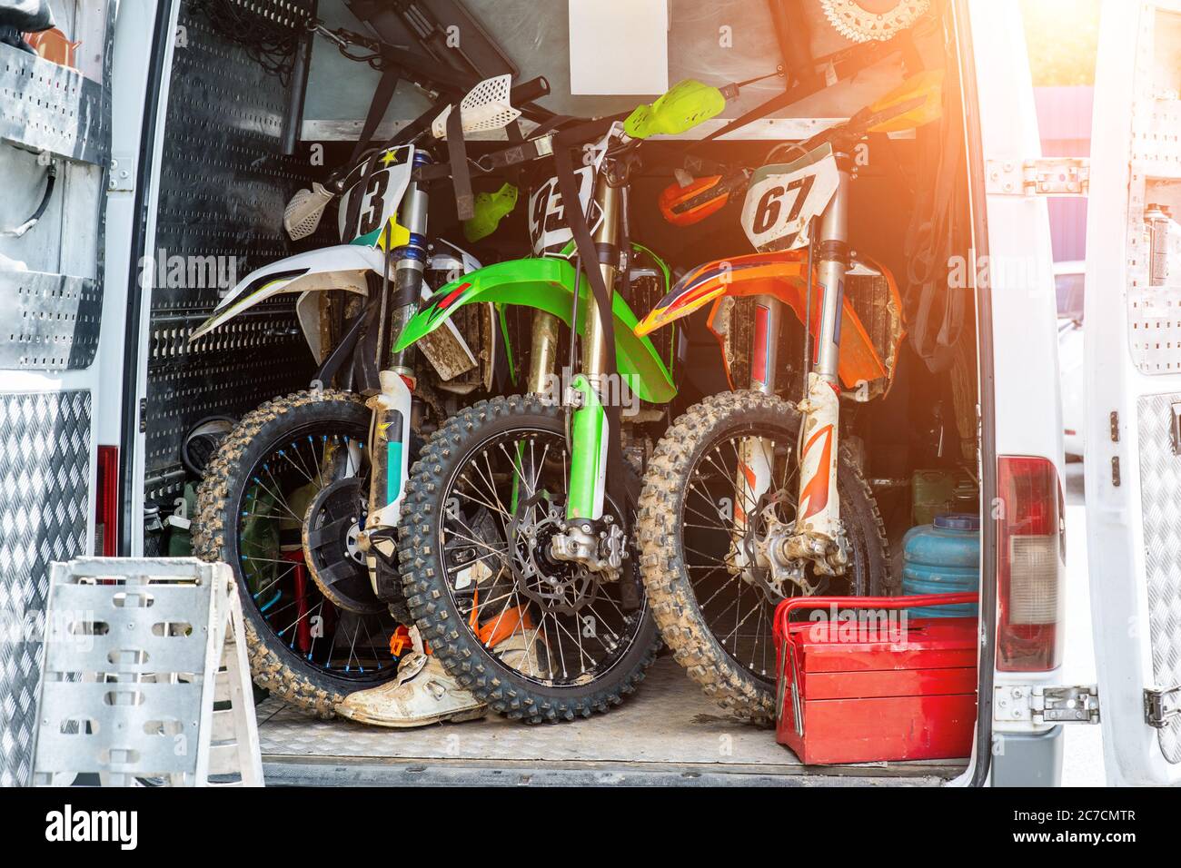 Tre moto da motocross sportive sporche e luminose si levano in coda al furgone di assistenza tecnica nel campo di squadra durante il campionato fuoristrada estremo Foto Stock