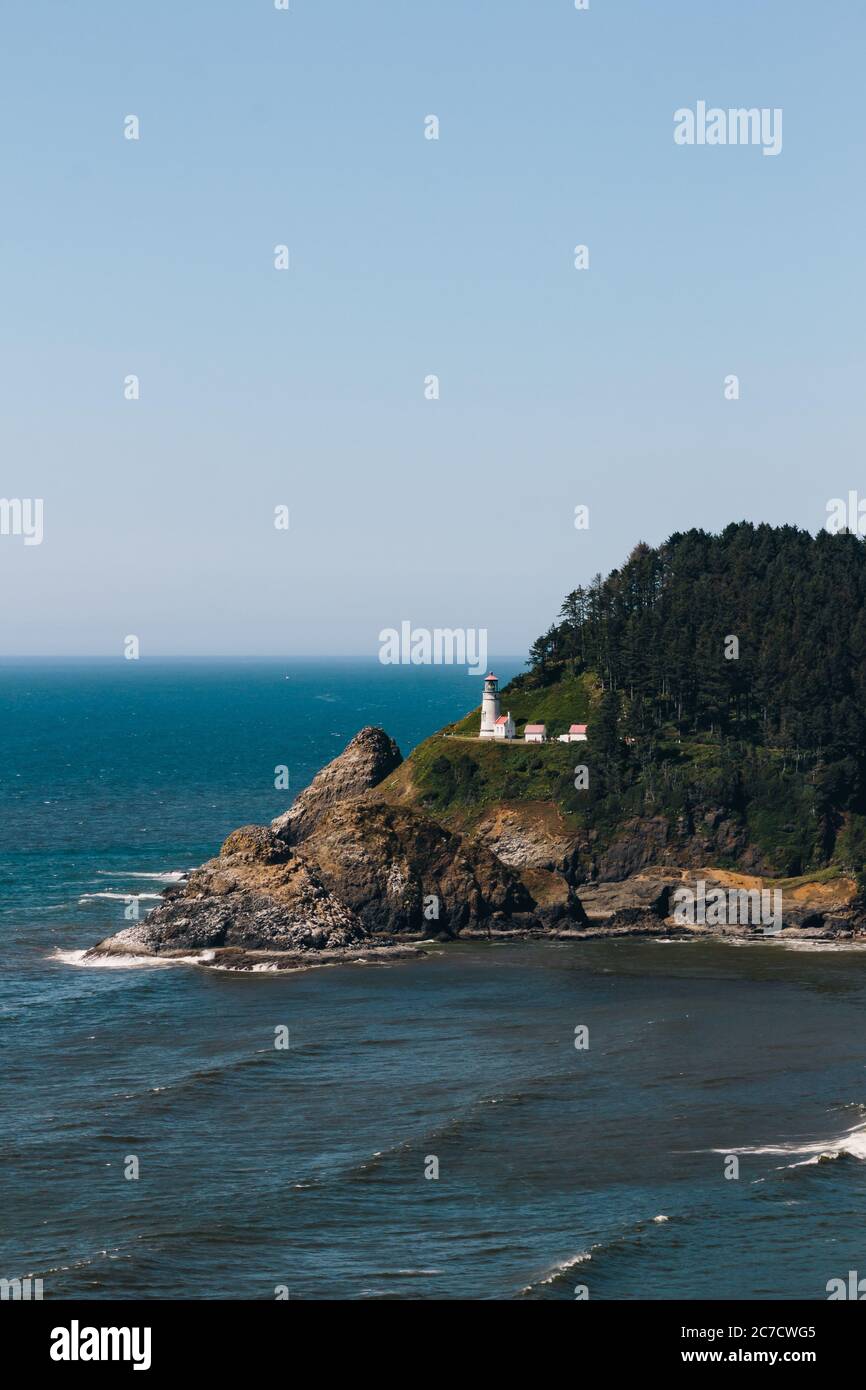 Scatto verticale di un faro su una scogliera circondata da alberi sul mare sotto un cielo blu Foto Stock