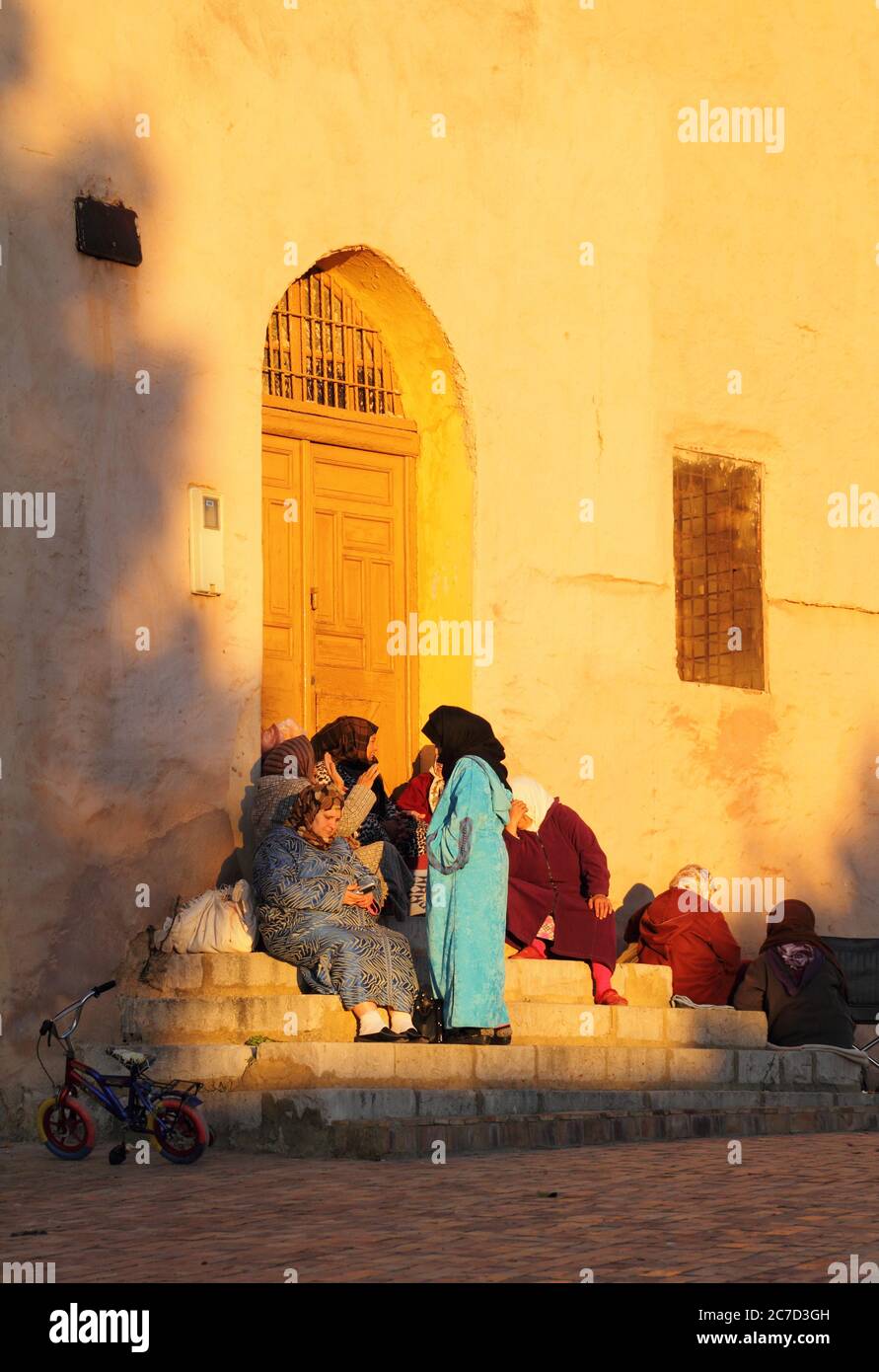 Un gruppo di donne marocchine, tipicamente vestite, seduti su gradini nel tardo pomeriggio del sole invernale. 22 dicembre 2013 a Meknes, Marocco. Sito UNESCO. Foto Stock