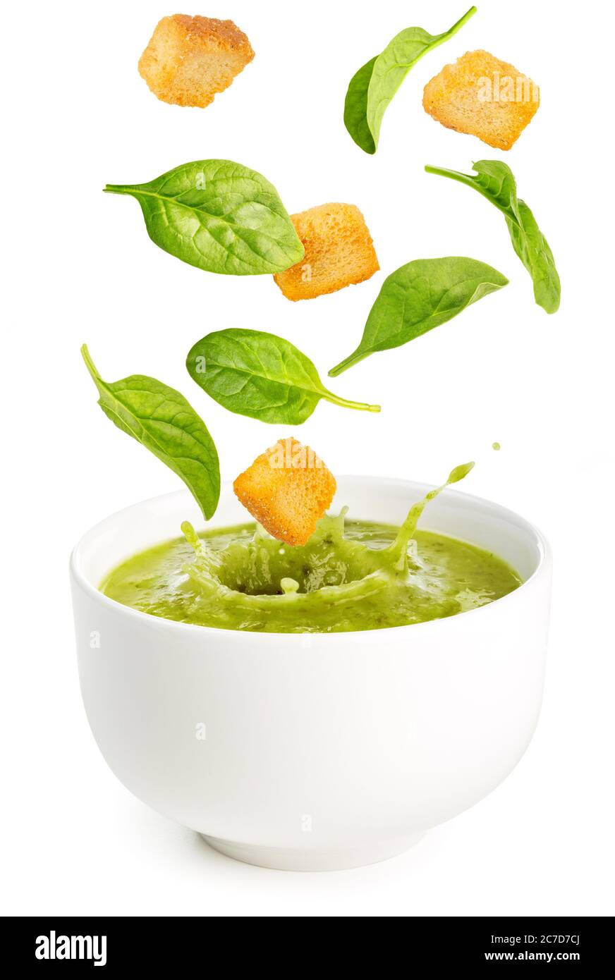 foglie di spinaci e crostini che cadono in una zuppa isolata su bianco Foto Stock