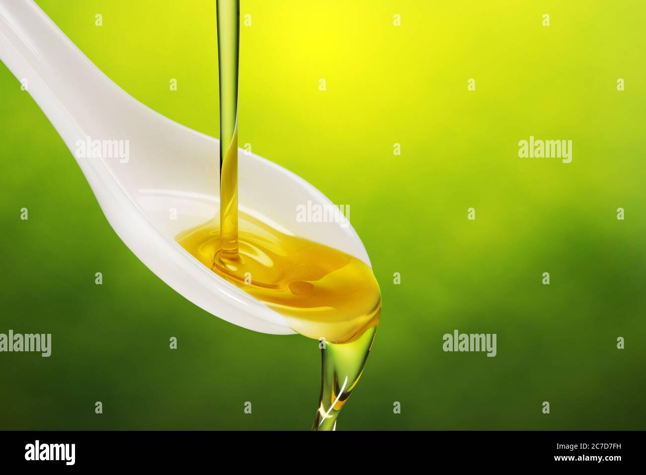olio extravergine di oliva versato in un cucchiaio traboccante su fondo verde Foto Stock