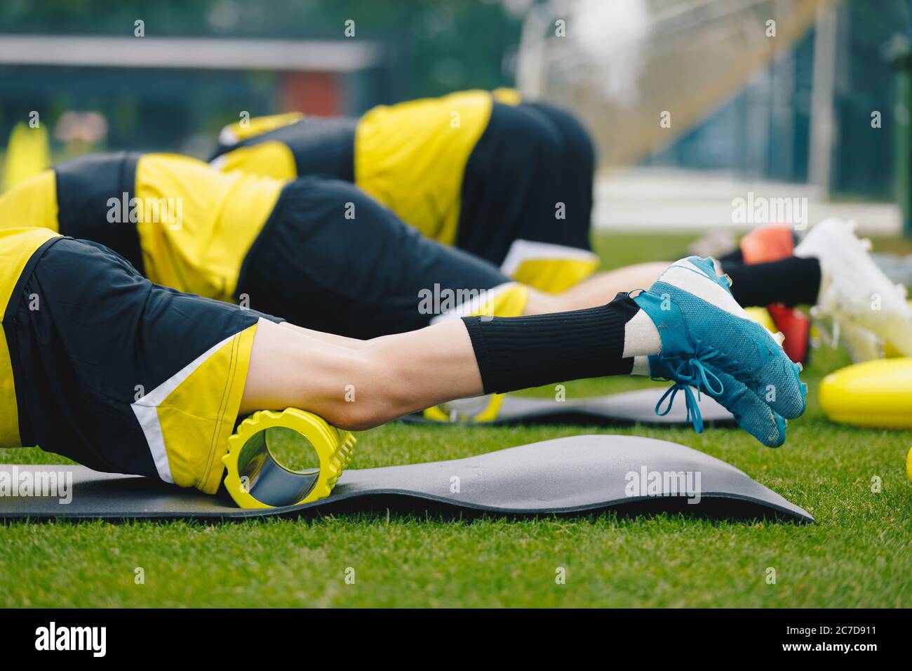 Laminazione della schiuma. Gruppo di giovani giocatori di calcio in scarpe da calcio usando il rullo in schiuma da training sulla sessione di allenamento. Stretching e riscaldamento dei muscoli Foto Stock