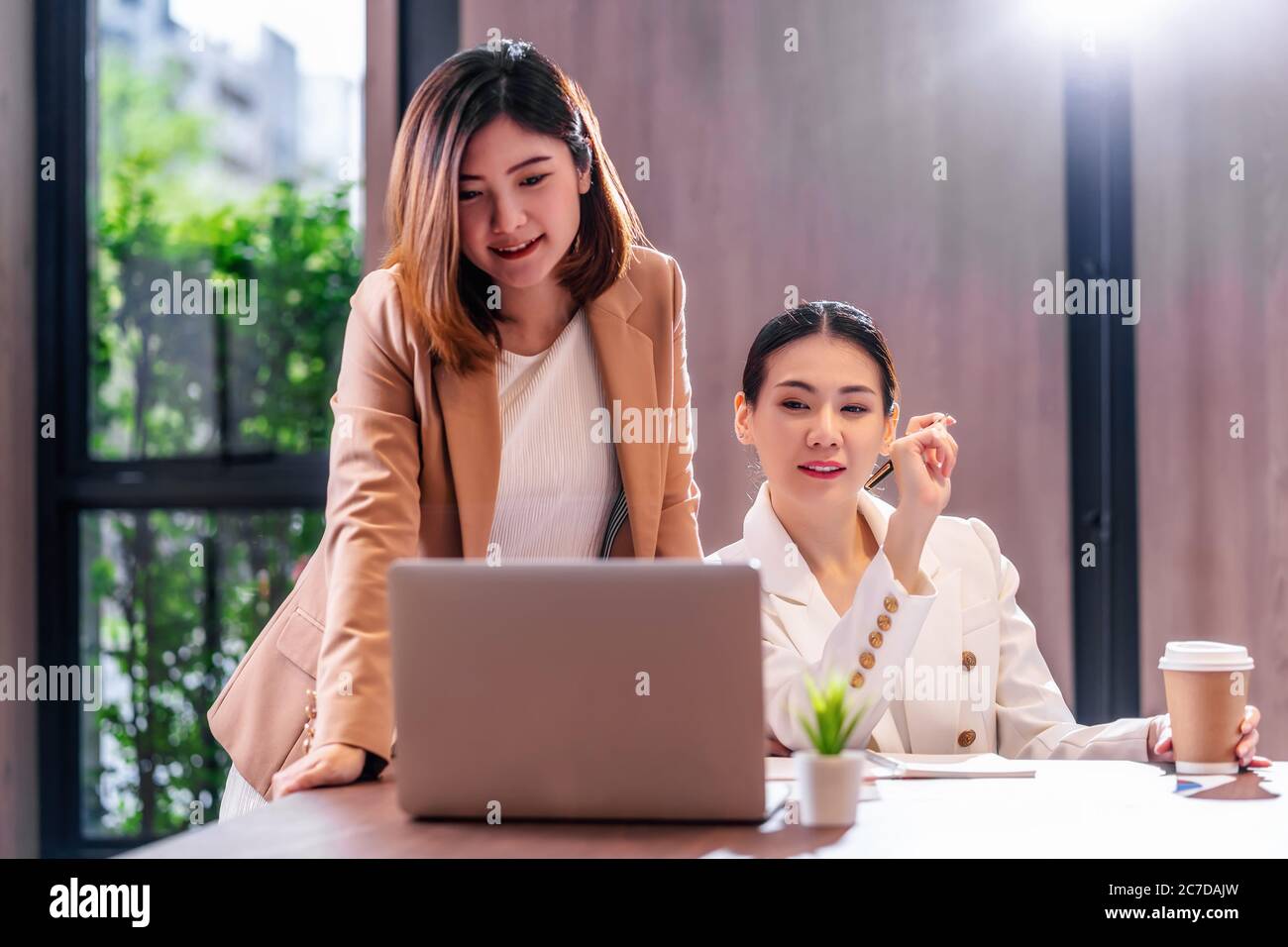Due donne d'affari asiatiche che lavorano con il business partner tramite computer portatile tecnologico in una moderna sala riunioni, ufficio o spazio di lavoro, pausa caffè, partner Foto Stock