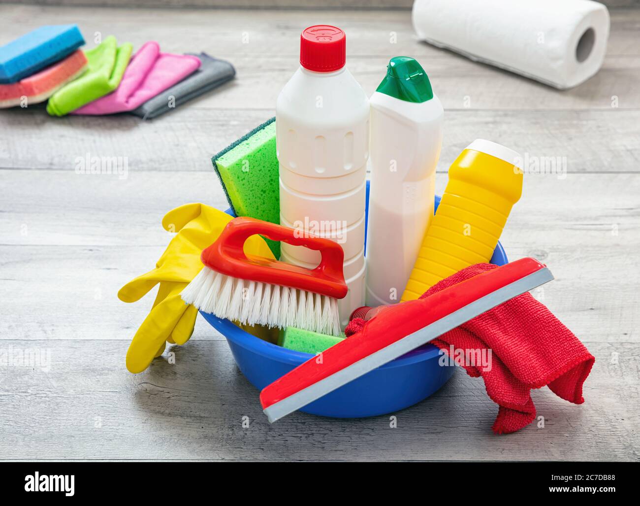 Prodotti per la pulizia sul pavimento, sfondo interno casa. Bottiglie di detergente chimico in un recipiente blu. Pulizia sanitaria domestica o aziendale Foto Stock