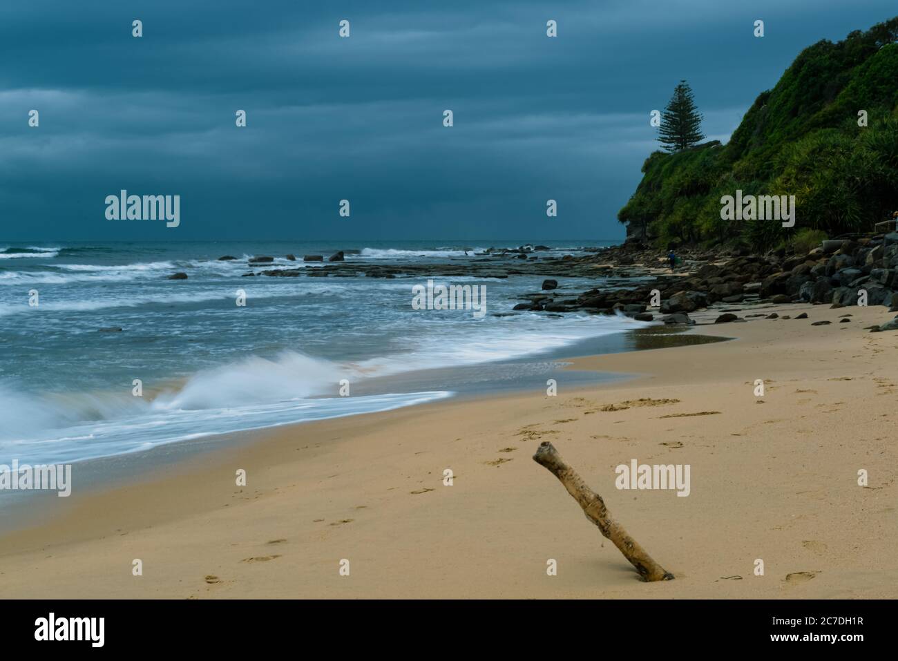 Bellissimo scatto di una spiaggia vicino a una scogliera boscosa sotto un cielo nuvoloso Foto Stock