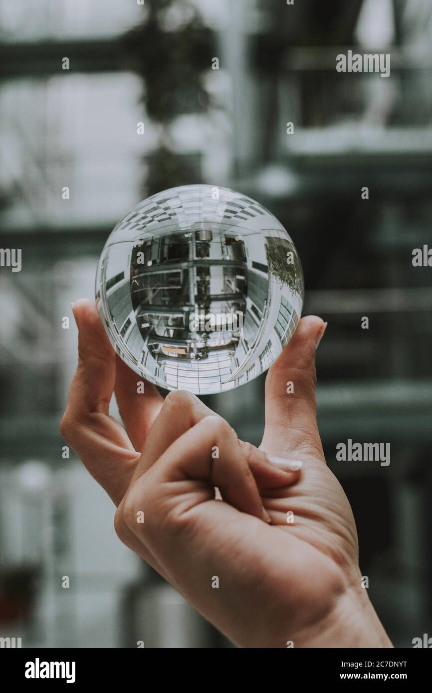 una persona che tiene una sfera di cristallo trasparente con il riflesso di un edificio Foto Stock