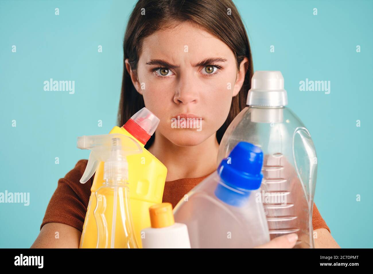Primo piano ragazza che tiene i detergenti di plastica vuoti in mani anglioso guardando in macchina fotografica su sfondo colorato isolato Foto Stock
