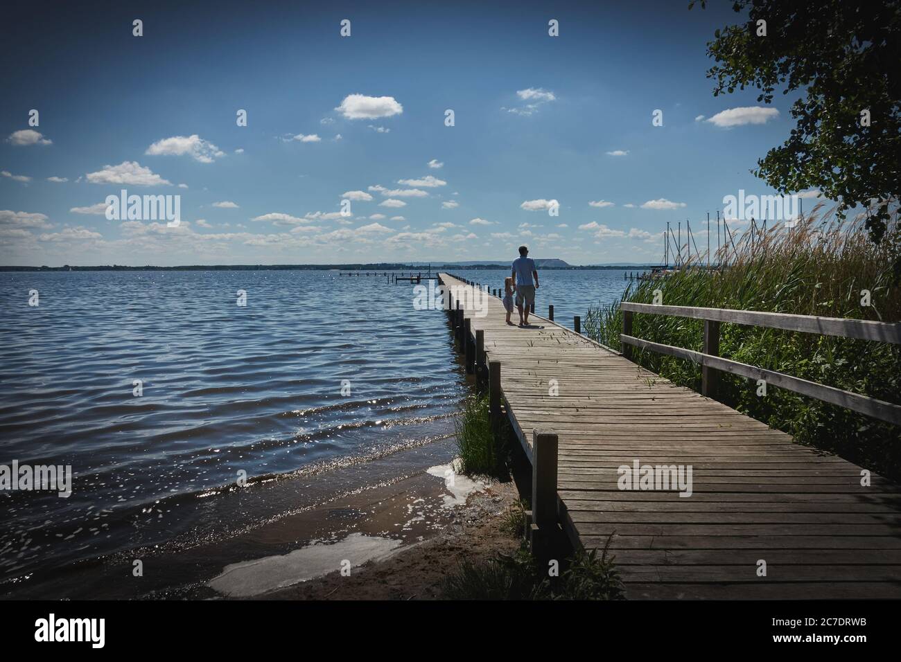 Steinhude, Germania, 29 maggio 2020: Padre con bambino in mano cammina su un lungo molo di legno attraverso il lago, vignetta scura Foto Stock