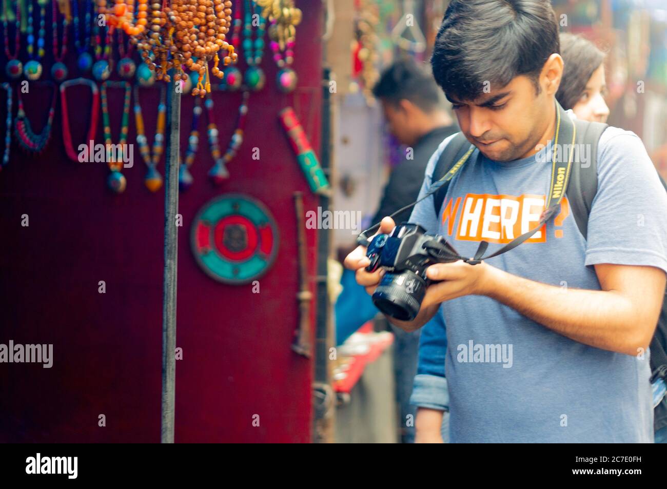 Giovane fotografo indiano che scatta guardando la sua macchina fotografica nel mezzo del mercato nella città collinare di mcleodganj in India himachal pradesh Foto Stock