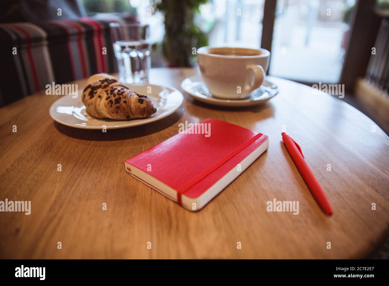Una nota rossa e una penna rossa sono sul tavolo in un caffè, una tazza di caffè e un croissant sullo sfondo Foto Stock