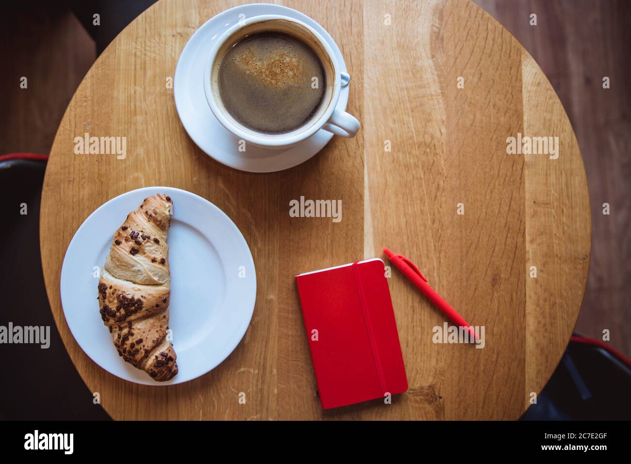 Una nota rossa e una penna rossa sono sul tavolo in un caffè, una tazza di caffè e un croissant Foto Stock
