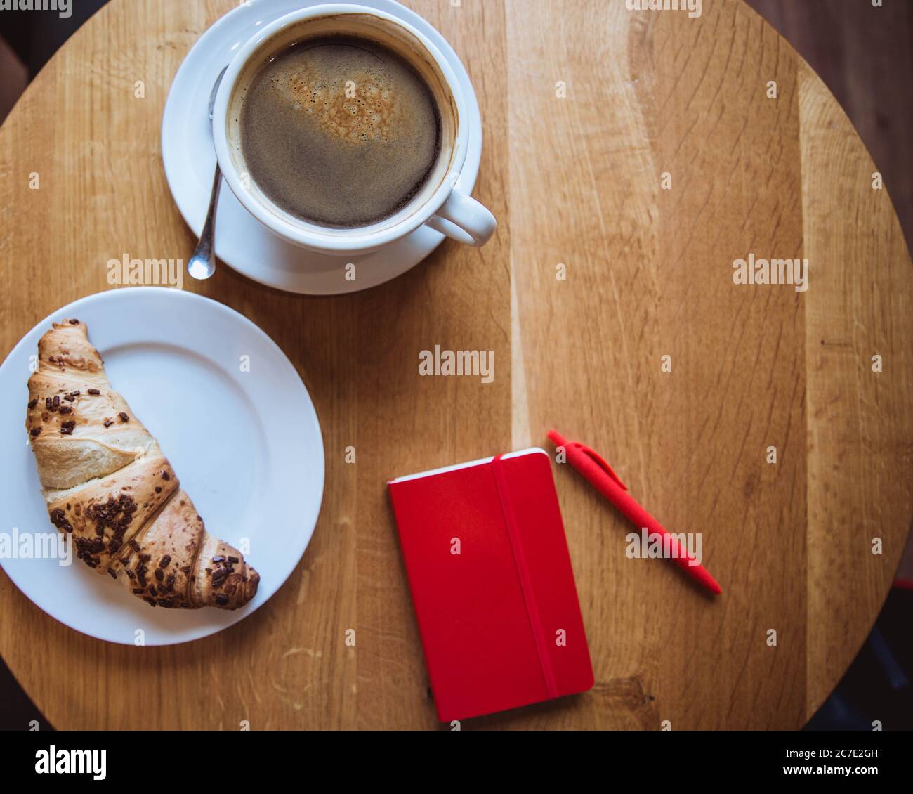 Una nota rossa e una penna rossa sono sul tavolo in un caffè, una tazza di caffè e un croissant Foto Stock