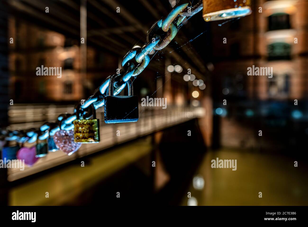 Primo piano focalizzato poco profondo di una catena vicino a un ponte con lucchetti attaccati ad esso come simbolo di amore Foto Stock