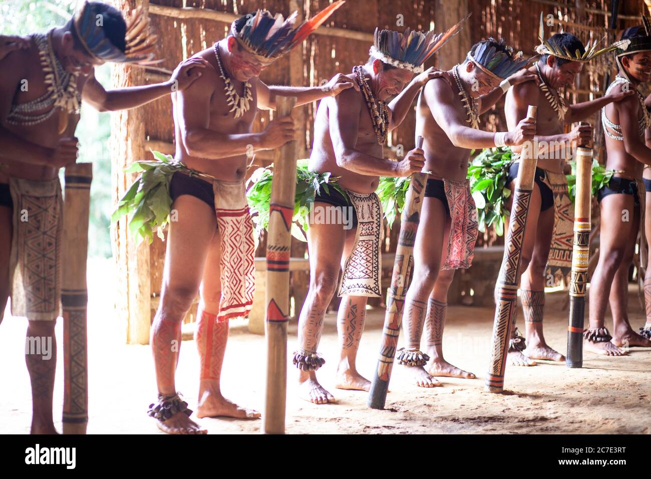 Gli uomini indigeni amazzonici eseguono una tradizionale cerimonia tribale con bastoni cerimoniali, indossando copricapi piumati e vernice per il corpo, celebrando il loro Foto Stock