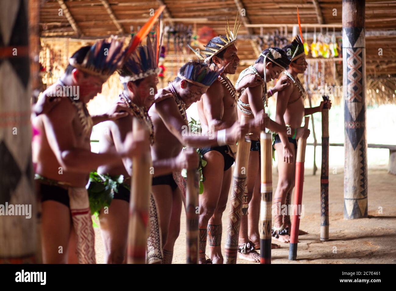 Gli uomini indigeni amazzonici eseguono una tradizionale cerimonia tribale con bastoni cerimoniali, indossando copricapi piumati e vernice per il corpo, celebrando il loro Foto Stock
