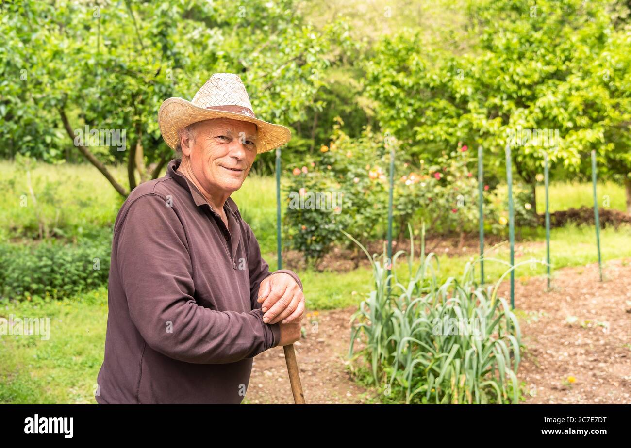 Ritratto di un uomo anziano sorridente che indossa un cappello nel suo orto in primavera. Foto Stock