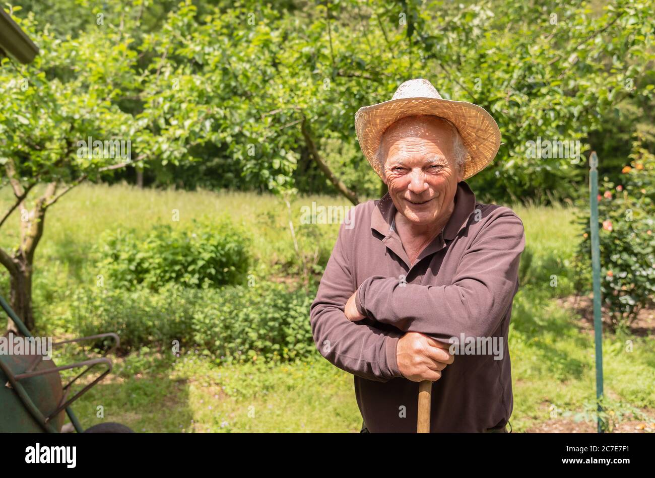Ritratto di un uomo anziano sorridente che indossa un cappello nel suo orto in primavera. Foto Stock