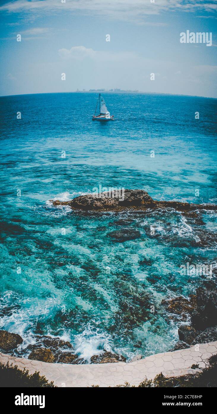 Scatto verticale di una barca a vela isolata nel bel ondulato mare sotto il cielo nuvoloso mozzafiato Foto Stock