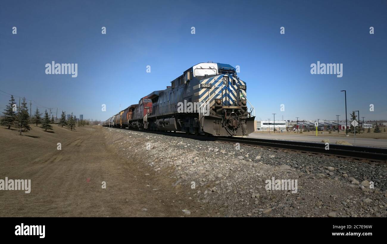 Motori in treno blu e rosso che traina auto da carico miste con edifici sullo sfondo Foto Stock