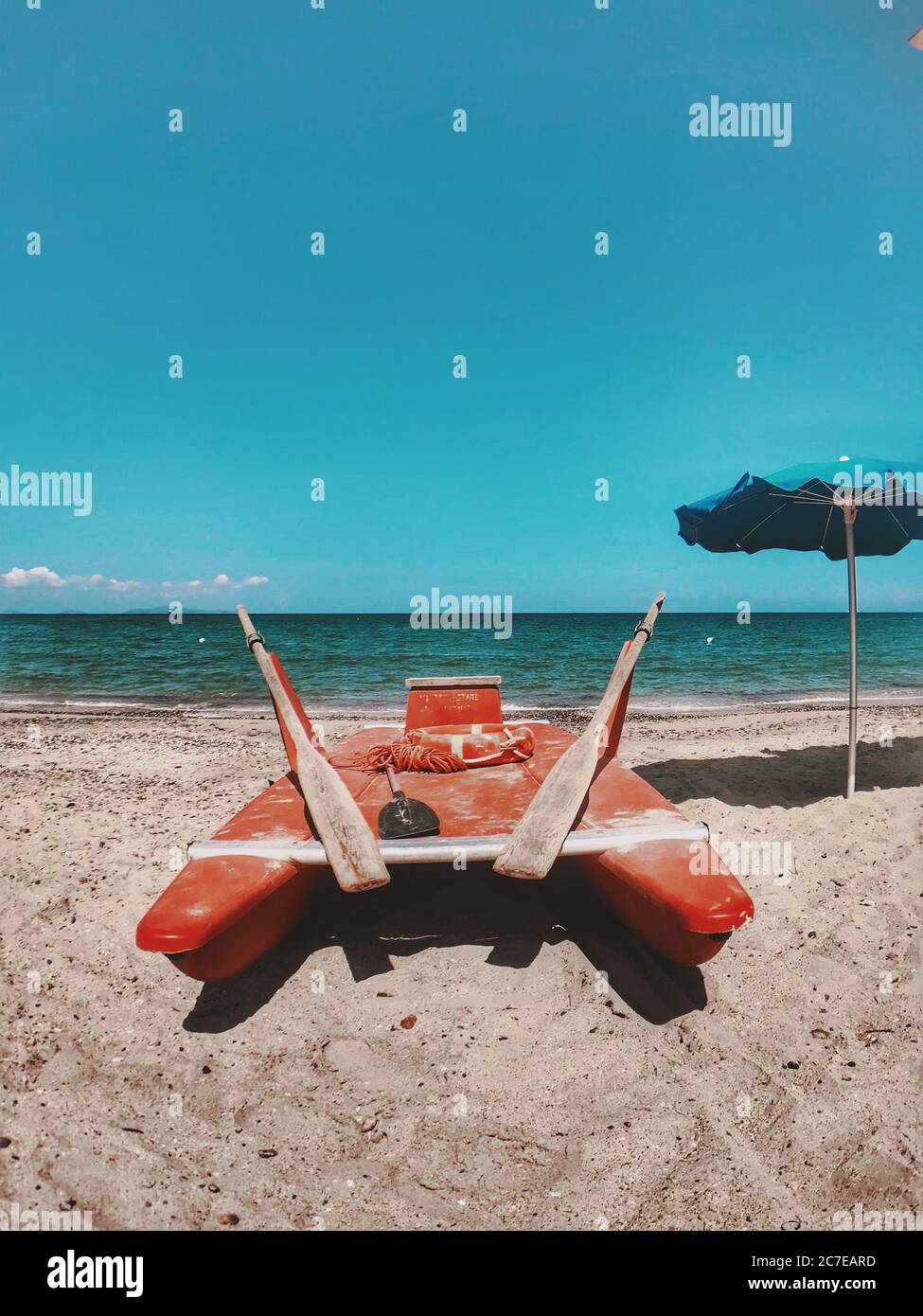 Una moto d'acqua rossa vicino ad un ombrello blu sulla spiaggia con il bel mare sullo sfondo Foto Stock