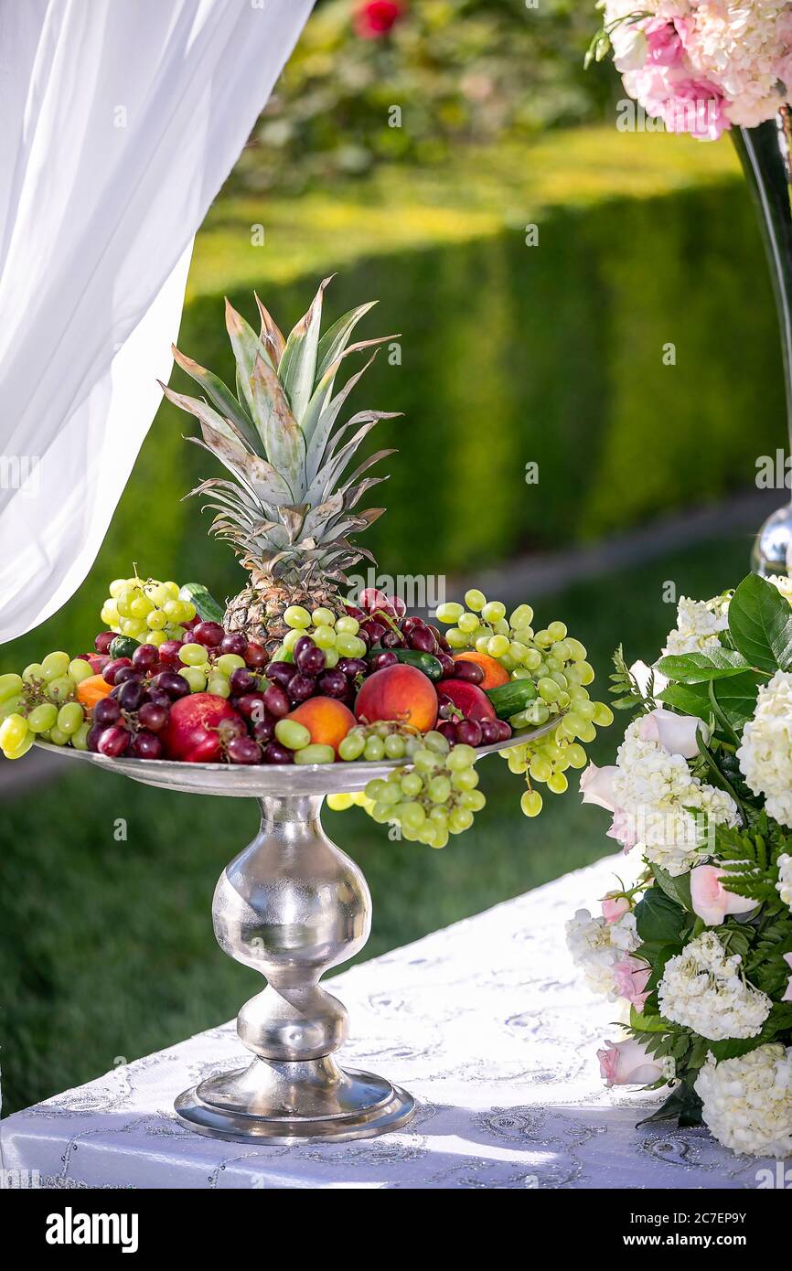 Decorazioni in stile weddiig all'aperto e vassoio d'argento pieno di uva, ciliegie, ananas e vari altri frutti a buffet Foto Stock