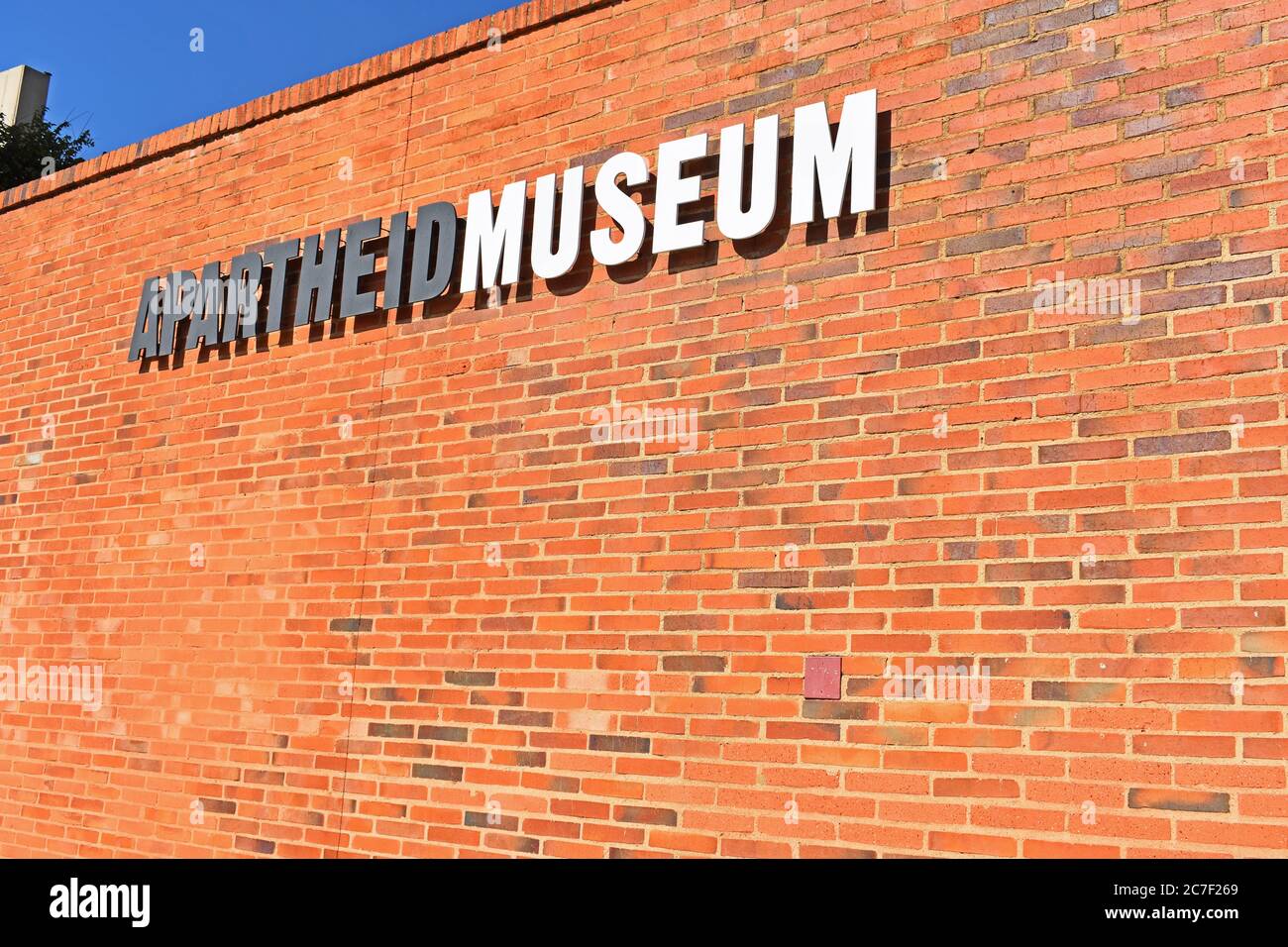 Un muro di mattoni rossi con un cartello per il Museo dell'Apartheid a Johannesburg, Sudafrica. Foto Stock