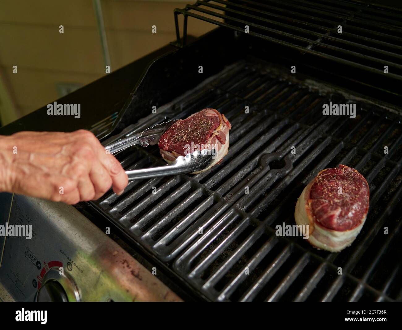 Cuoca donna o chef con pinze che maneggiano una bistecca tagliata a filetto spesso su una griglia a gas, grigliando la bistecca per mettere il cibo sul tavolo. Foto Stock