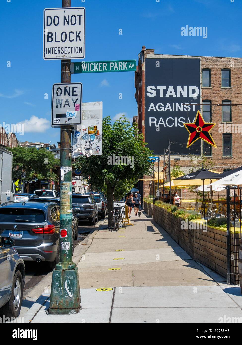 Vista a nord su Damen Avenue, quartiere di Wicker Park di Chicago. Ristorante Big Star sulla destra. Opporsi alla bandiera del razzismo sull'edificio. Foto Stock