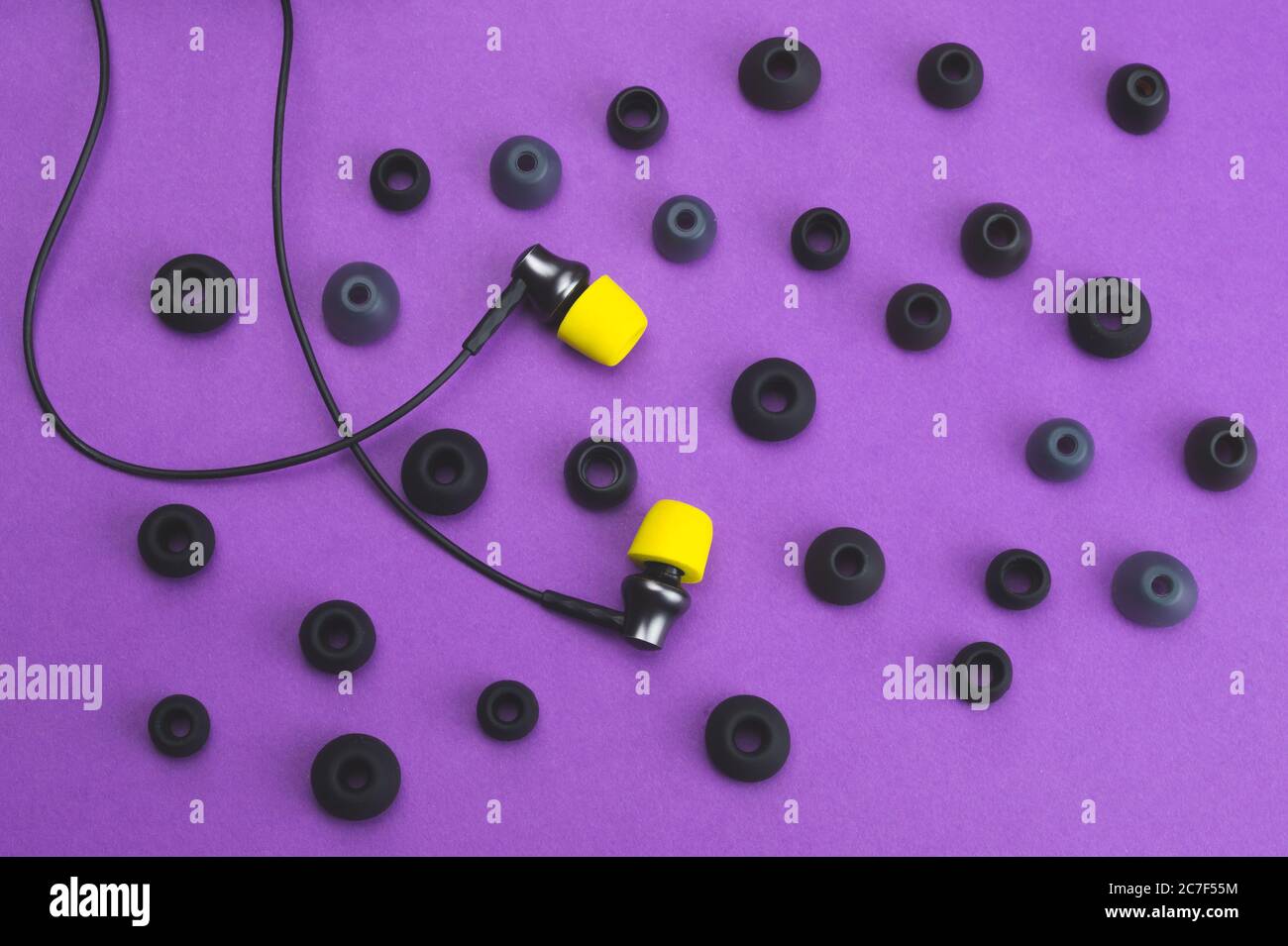 Concetto di individualità. Auricolari con cuscinetti gialli tra gli inserti grigi. Cuffie intrauricolari. Stile moderno. Apparecchiature audio Foto Stock