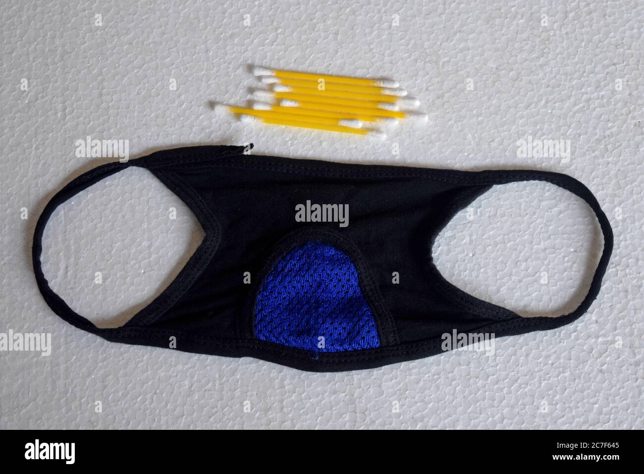 maschera nera su sfondo bianco e alcuni bastoncini di cotone per la pulizia delle orecchie. Foto Stock