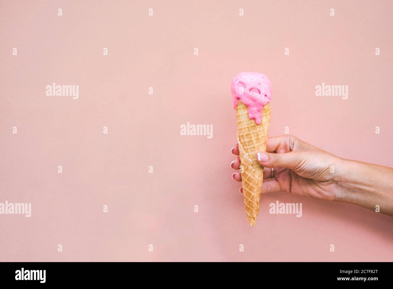 Ragazza mano tenendo fuso rosa fragola gelato cono su sfondo rosa. Foto Stock